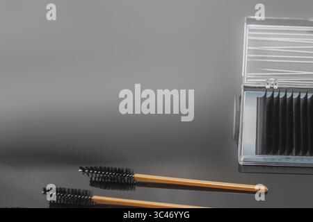 Close-up of eyelash extensions in a transparent case with professional brushes on a glossy black background. Beauty tools for lash extension procedure Stock Photo