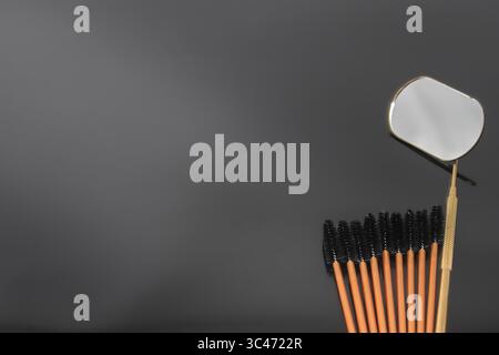 Disposable eyelash brushes and a metal mirror on a black background. Professional tools for eyelash extension, makeup and beauty salon procedures. Stock Photo