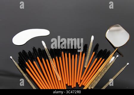 Disposable eyelash brushes, micro brushes, under eye patch and a metal mirror on a black background. Professional tools for eyelash extensions, beauty Stock Photo