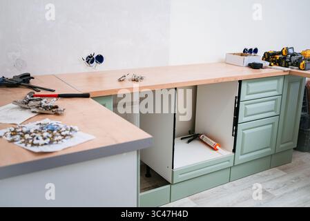 Carpenters are assembling a new kitchen in an apartment, installing cabinets, countertops, and various tools and materials are scattered around the workspace Stock Photo