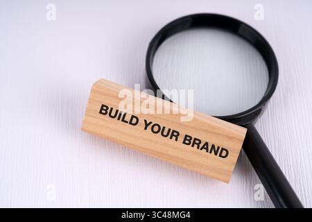 Magnifying glass and text build your brand text on wooden block business concept Stock Photo