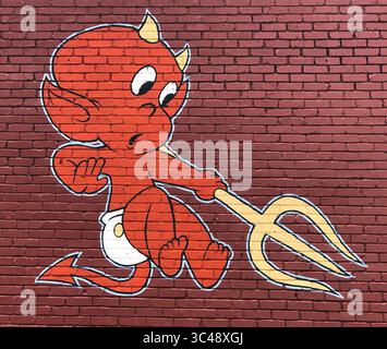 Playful street art in Asheville, North Carolina shows a mischievous baby devil in diapers, grinning wide and pointing the way to hell. Stock Photo