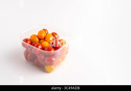 Fresh red and yellow cherry tomatoes in a clear plastic container on white background. Stock Photo