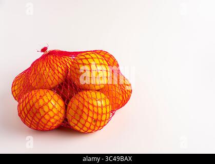 Bright oranges in red mesh bag, isolated on white background. Stock Photo