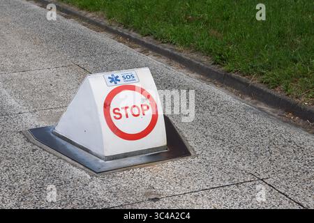 A "STOP" sign with an "SOS Toegang" (SOS Access) logo on a triangular white marker, set into the ground near a grassy area, indicating an emergency ac Stock Photo