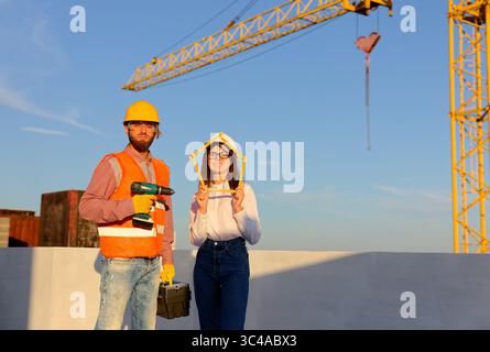 Construction workers are posing at building site holding folding ruler and cordless drill with crane in background Stock Photo