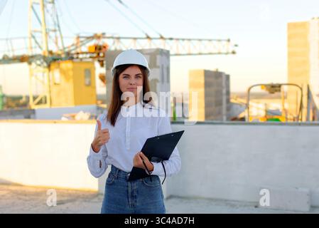 Architect pointing at a blank document on a clipboard, standing on a rooftop with a construction worker, during a site inspection Stock Photo