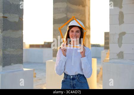 Confident female architect holding a folding ruler while inspecting a building under construction at sunset Stock Photo