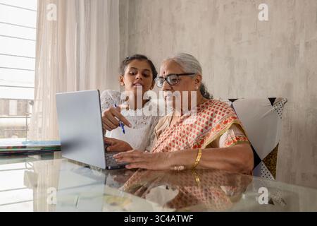 Indian Granddaughter Teaching Senior Woman (Grandmother) to Use Laptop at Home. Working Together on School Assignment using laptop. Stock Photo