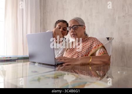 Indian Granddaughter Teaching Senior Woman (Grandmother) to Use Laptop at Home. Working Together on School Assignment using laptop. Stock Photo