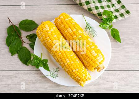 Two boiled corn cobs with dill on a white plate. Stock Photo