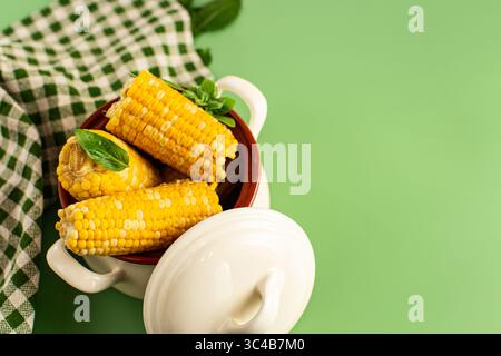 Hot corn cobs with greens on a green background. Stock Photo