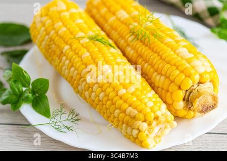 Two boiled corn cobs with dill on a white plate. Stock Photo