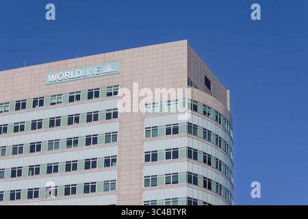 A modern, multi-story office building with many windows under a bright blue sky, featuring the "WORLDLINE" logo prominently displayed on its upper fac Stock Photo