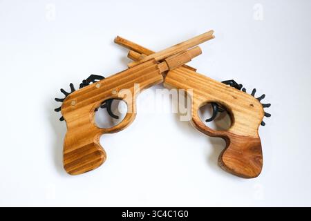 Two handcrafted wooden guns with distinct grain patterns crossed in an X shape. Shot on white background Symbolic and artistic composition. Stock Photo