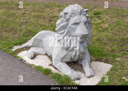 An angular, geometric concrete lion sculpture,  rests on a concrete slab amidst green grass and a paved path, showcasing modern public art. Utrecht, N Stock Photo