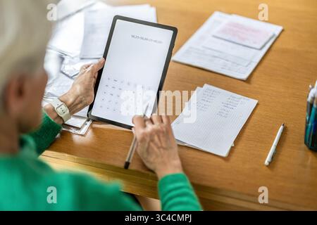 Senior woman using calculator app on digital tablet at table Stock Photo