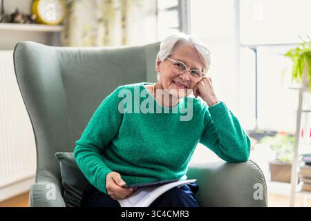 Senior woman using digital tablet while sitting in armchair at home Stock Photo