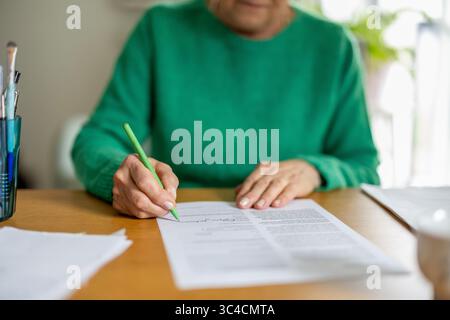 Unrecognizable senior woman signing a document, close-up Stock Photo