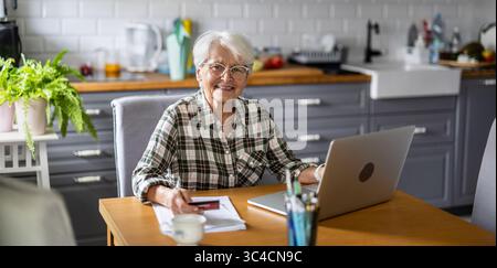 Senior woman using laptop and credit card for online shopping at home Stock Photo