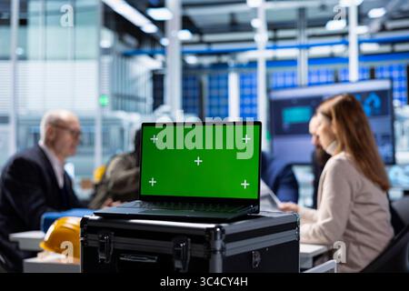 Investors evaluating factory production efficiency using green screen laptop before investing. Shareholders meeting with industrial plant managers to understand business model, using mockup notebook Stock Photo