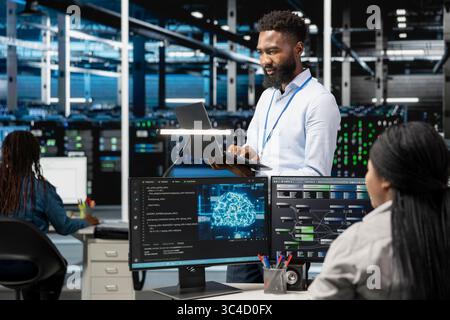 Data center programmer using artificial intelligence neural networks technology. African american man working in server farm using AI programming language on computer, configuring specialized hardware Stock Photo