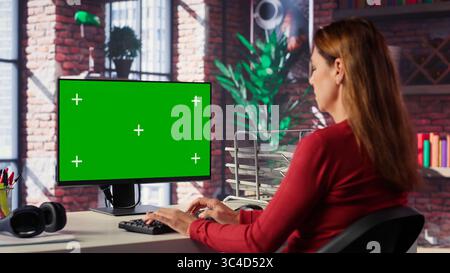 Confident woman solves freelancing tasks at copy space desktop, browsing the internet pages at her home office. Mature focused person self employed doing her job remotely. Camera A. Stock Photo