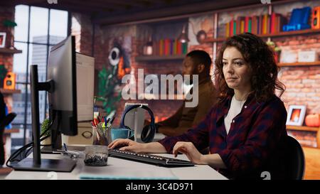 Smiling woman using programming languages on PC in IT startup office to build applications. Upbeat programmer using computer in software development agency to code, camera B Stock Photo
