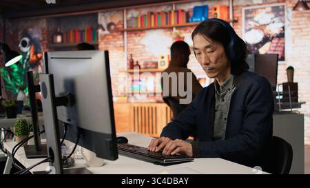 Senior admin coding advanced AI algorithm in startup office, refining machine learning models to enhance automation, wearing headphones. CTO manager listening music and coding, camera A Stock Photo