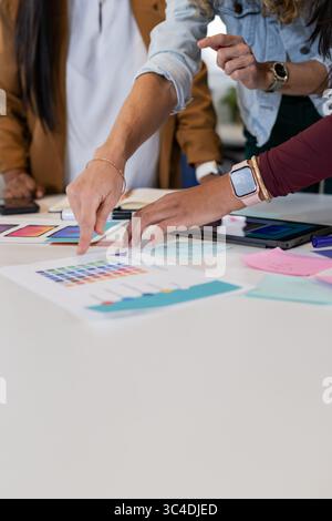 Diverse female team in business attire examining color swatches and tablets on white office table Stock Photo