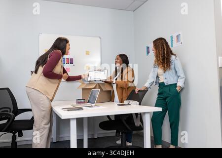 Diverse female colleagues exchanging tablet while reviewing laptop, notes and whiteboard in office Stock Photo