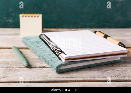 Notebooks, pens and stickers on wooden table near green wall Stock Photo