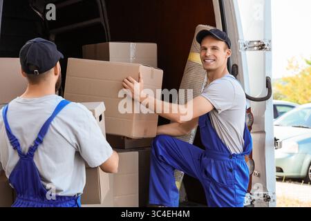 Male movers unloading boxes from car outdoors Stock Photo