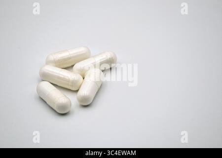 A cluster of five white, opaque capsules arranged on a simple white background, suitable for medical or health-related contexts. Stock Photo