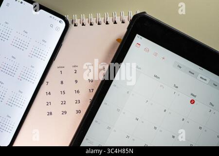 Flatlay of smartphone and tablet displaying digital calendars beside a paper calendar. Perfect for productivity content, tech blogs, scheduling apps, Stock Photo