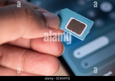 Hand holding a SIM card with blurred smartphone in background. Great for tech tutorials, mobile service promotions, repair guides, or telecommunicatio Stock Photo