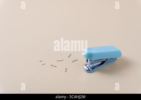 A desktop stapler surrounded by scattered staples on a table. Captures a busy, slightly messy work or office scene with close up details Stock Photo