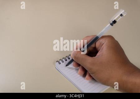A hand writing with a ballpoint pen on an open notebook, captured close-up. The scene shows a focused moment of note taking or journaling Stock Photo