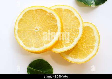 Three bright, juicy slices of fresh lemon, artfully arranged on a clean white background with scattered green leaves, ready for drinks or garnish. Stock Photo