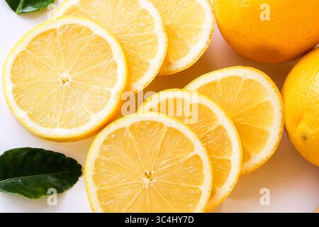 A close-up of translucent lemon slices, revealing their juicy texture and bright yellow color, with a hint of two whole lemons in the background. Stock Photo