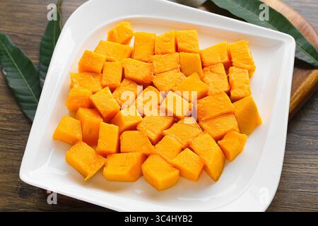 Closeup of a plate of freshly cut mango cubes served on a white dish over a wooden table. A vibrant tropical snack rich in flavor and color. Stock Photo