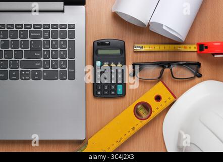 Creative layout of architects with roll drawings, architectural project plan, engineering tools and stationery, laptop on table, workspace. Top view. Stock Photo
