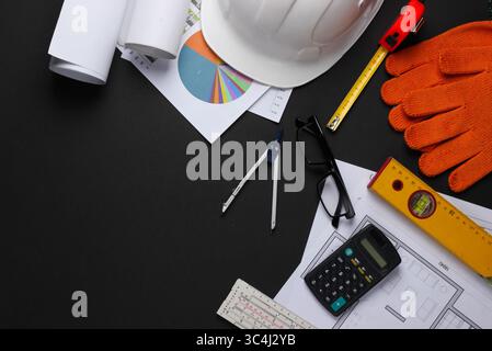 Creative layout of architects with roll drawings, architectural project plan, engineering tools and stationery on black background, workspace. Top vie Stock Photo
