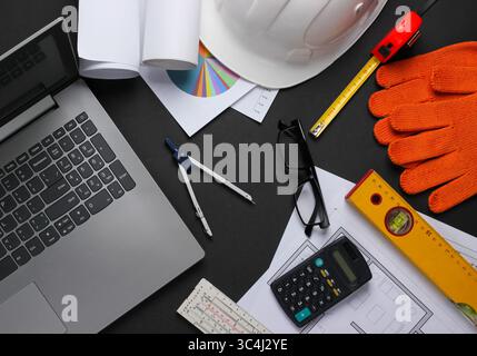Creative layout of architects with roll drawings, architectural project plan, engineering tools and stationery, laptop on black background, workspace. Stock Photo