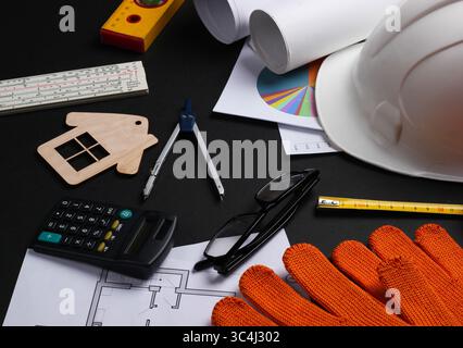 Creative layout of architects with roll drawings, architectural project plan, engineering tools and stationery on black background, workspace. Stock Photo