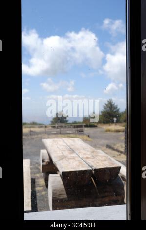 focus on dirty window glass and blurred scene with rustic wooden table and white clouds on background, Galvarina, Etna Park, Sicily, Italy Stock Photo