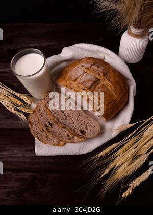 Rustic loaf of bread with slices and a glass of milk on a wooden table with wheat ears – cozy farmhouse breakfast scene Stock Photo