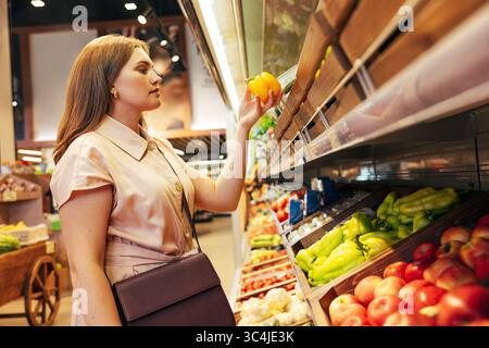 Young woman customer holding yellow papper while standing at shelves in grocery store Young woman customer holding yellow papper while standing at she Stock Photo