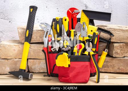 Belt bag with various hand tools leaning on an old bricks on a wooden table. Selective focus. Stock Photo