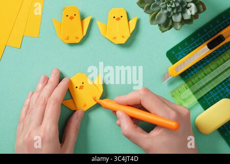 Making a simple Easter origami handicraft. Draw eyes and legs on the finished chicken. Around ready-made crafts chickens and tools for crafts Stock Photo